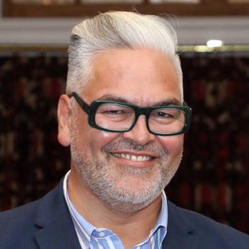 An image of playwright Victor Rodger wearing glasses and a suit, smiling