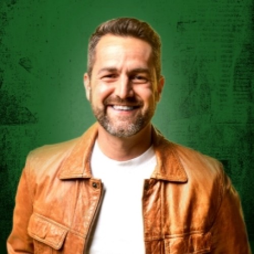 Comedian Ivan Aristeguieta Smiling warmly, wearing a brown leather jacket with a bright green background behind him