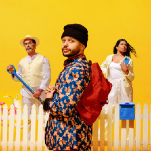 3 people stand in front of a yellow background, a white picket fence with a blue letterbox between. In the foreground a man with a black beanie, a colourful shirt and red back pack looks out at the camera. Behind him there is a man all in white holding a spade looking quizzically at the first man, and a women on the mans other side holding a blue phone, also dressed all in white. 