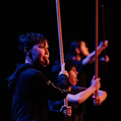 A young man carries a taiaha and gives his best pukana to the audience