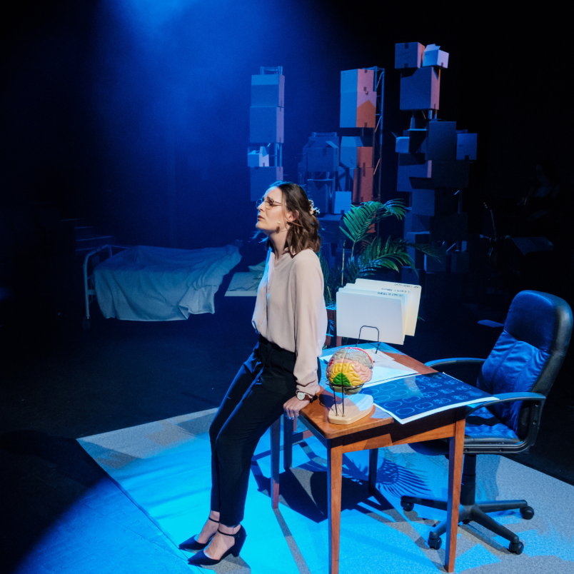 A woman on a stage singing. The set behind her implies a cosy family sitting room.