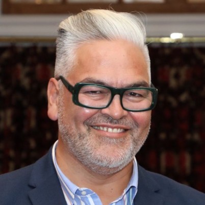 An image of playwright Victor Rodger wearing glasses and a suit, smiling