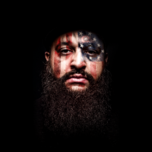 Close up on Comedian Azhar Usman with large beard, american flag projected across his face