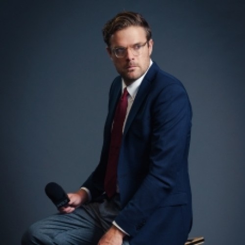 Comedia Guy Williams in a suit with a grey background