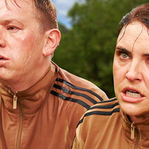 Actors Morgana O'Reily & Chris Parker in brown tracksuits, with a grim look on their facepuffing and sweating, spitting water out of their mouths