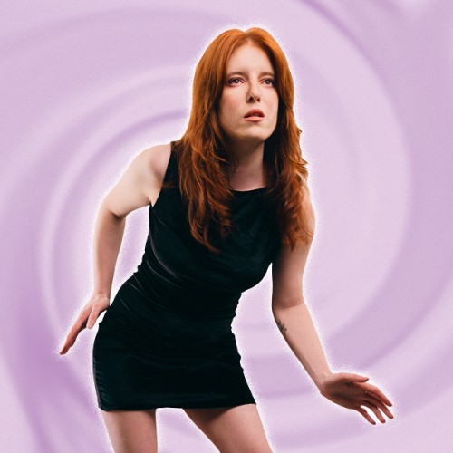 A photo of Renee Church standing at an odd angle with robotic arms agaisnt a pink background. She wears a black dress and has red hair