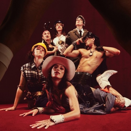 The cast of YMCĀ photographed from a low angle wearing different costumes