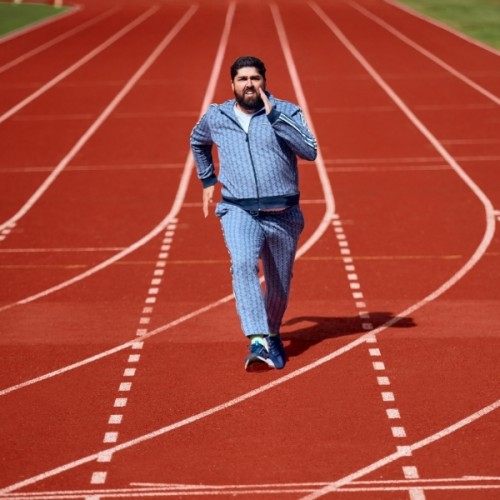 Rhys Mathewson photographed on a running track sprinting towards the camera. He wears a pale blue tracksuit.